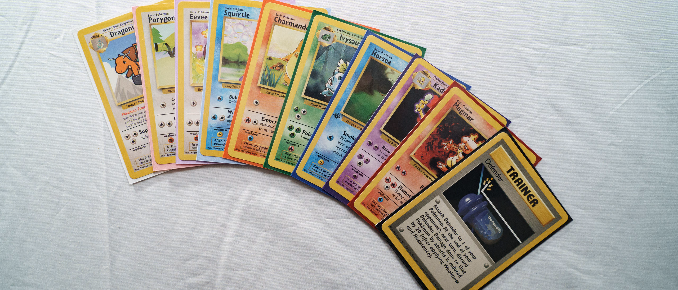 A fan of sleeved trading cards spread across a cloth backdrop
